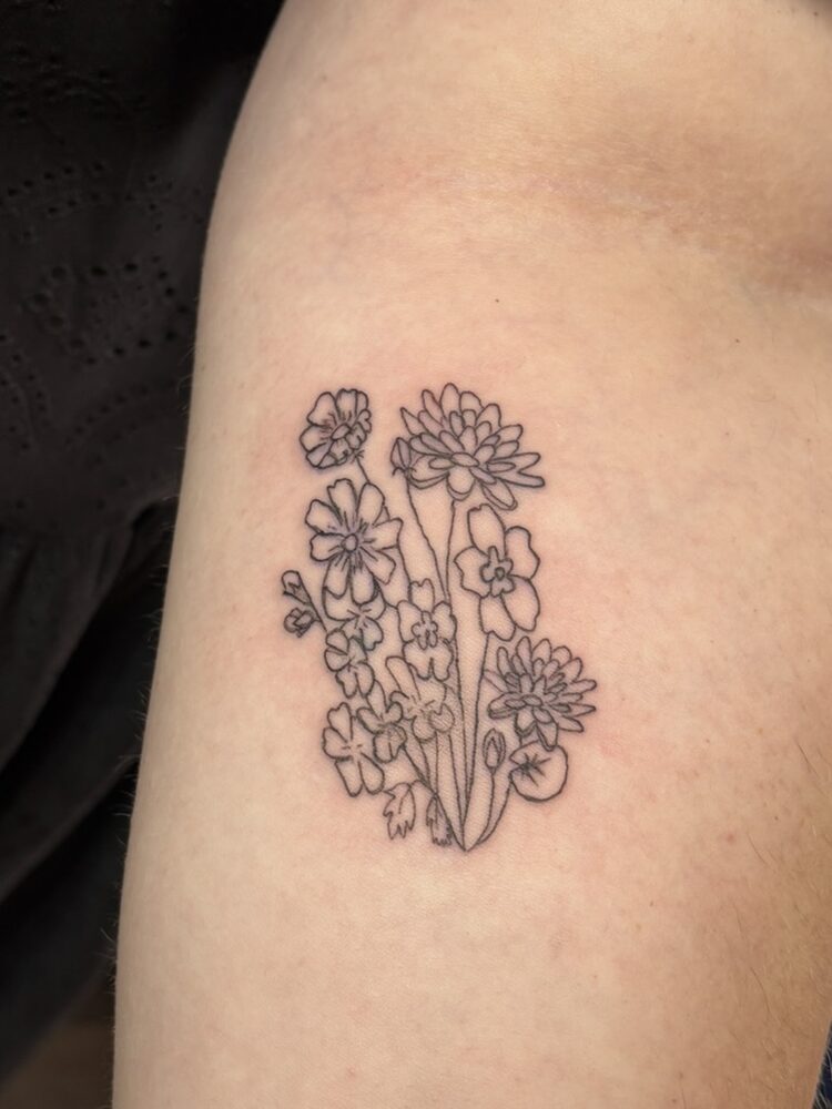 Fine line wildflower bouquet tattoo on the upper arm